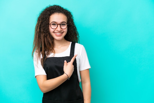 Serveur de restaurant femme arabe isolée sur fond bleu pointant vers le côté pour présenter un produit