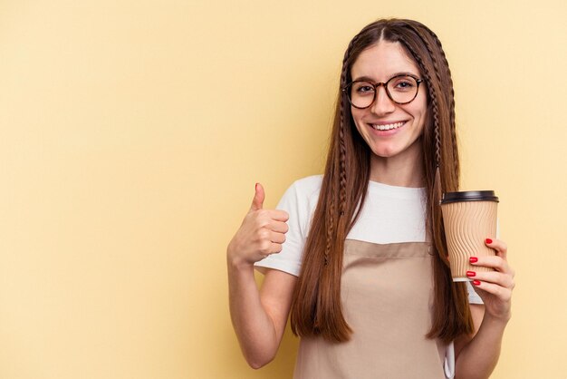 Serveur De Restaurant Femme Tenant Un Café à Emporter Isolé Sur Fond Jaune Souriant Et Levant Le Pouce Vers Le Haut