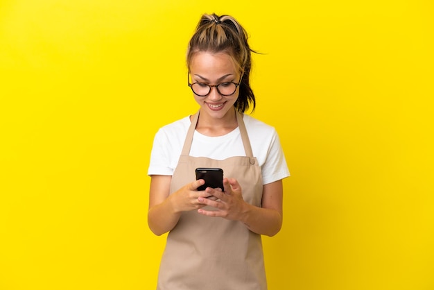 Serveur de restaurant fille russe isolée sur fond jaune envoyant un message avec le mobile