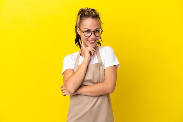 Serveur de restaurant fille russe isolée sur fond jaune avec des lunettes et souriant