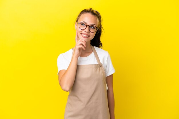 Serveur de restaurant fille russe isolée sur fond jaune pensant à une idée tout en levant les yeux