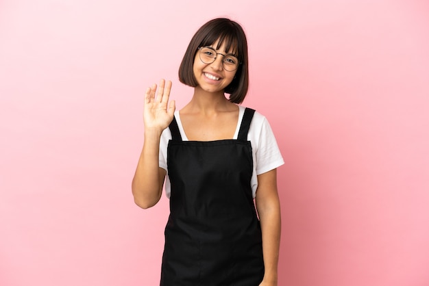 Serveur de restaurant sur fond rose isolé saluant avec la main avec une expression heureuse
