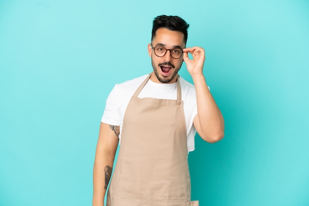 Serveur de restaurant homme caucasien isolé sur fond bleu avec des lunettes et surpris