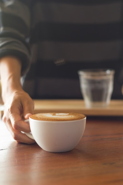 Serveur servant du café sur un mauvais éclairage. Centré sur une tasse de café.