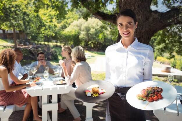 Serveur souriant tenant des assiettes d'aliments au restaurant