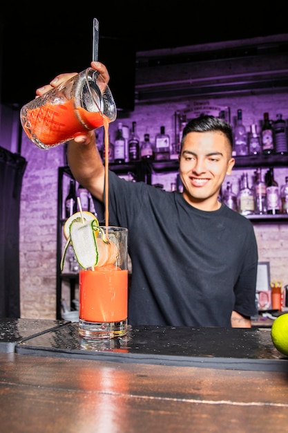 Un serveur souriant verse une boisson avec une passoire dans un verre à cocktail