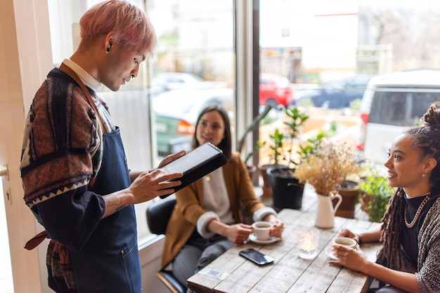 Un serveur avec une tablette numérique prenant des commandes de clients féminins dans un café