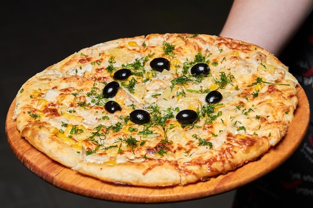 Photo le serveur tient une pizza au fromage ananas olives et herbes