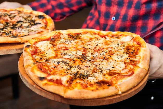 Le serveur tient une pizza avec des tomates au poivron salami et des cornichons au fromage, du bacon et des saucisses
