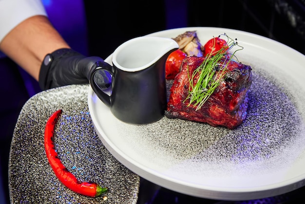 Le serveur tient un plat avec un steak avec des tomates en sauce et des piments rouges