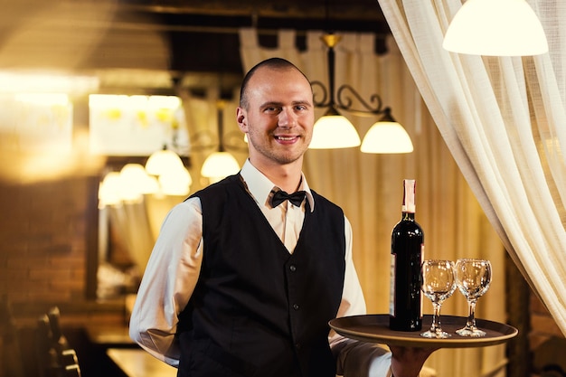 Le serveur en uniforme avec une serviette blanche offre aux visiteurs du vin au restaurant