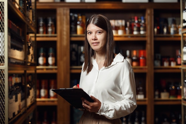 Un serveur de vin expérimenté tenant une tablette dans la cave sur une étagère de bouteilles de boissons alcoolisées