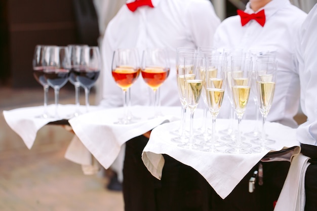 Photo les serveurs accueillent les clients avec des boissons alcoolisées. champagne, vin rouge, vin blanc sur plateaux.