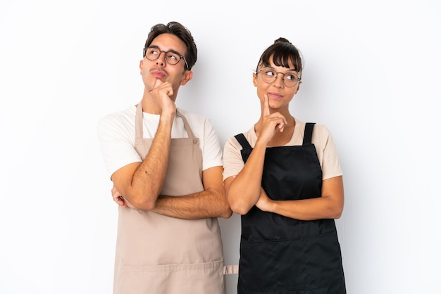 Serveurs de race mixte de restaurant isolés sur fond blanc pensant à une idée tout en levant les yeux