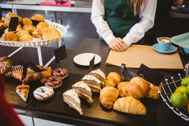 Serveuse debout derrière le comptoir avec beaucoup de pâtisseries