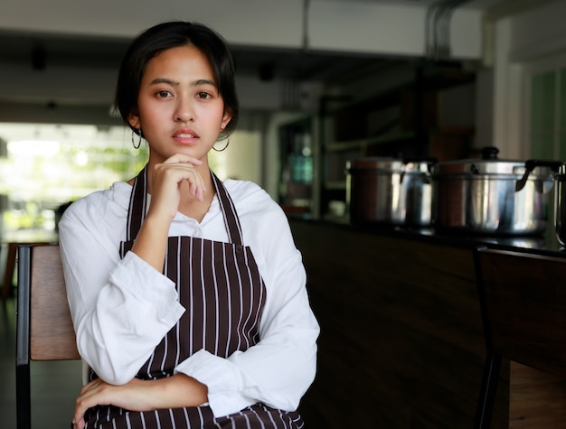 Serveuse ethnique confiante en tablier debout dans un café et regardant la caméra.