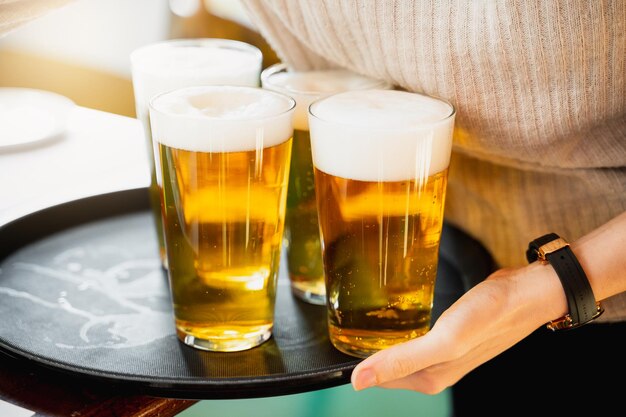 Serveuse méconnaissable servant trois verres de bière glacée avec de la mousse sur un plateau