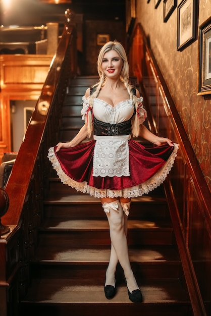 Serveuse Octoberfest en robe de style traditionnel sur l'escalier dans un pub vintage.