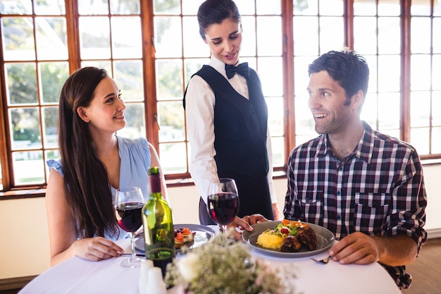 Serveuse servant une assiette sur la table des clients