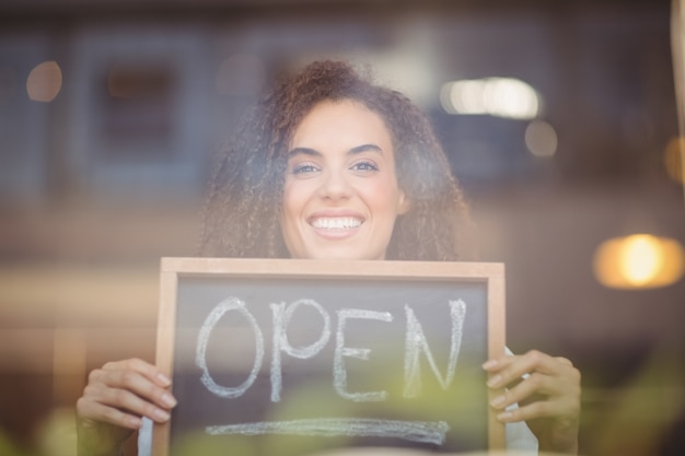 Photo serveuse souriante, montrant le tableau noir avec signe ouvert