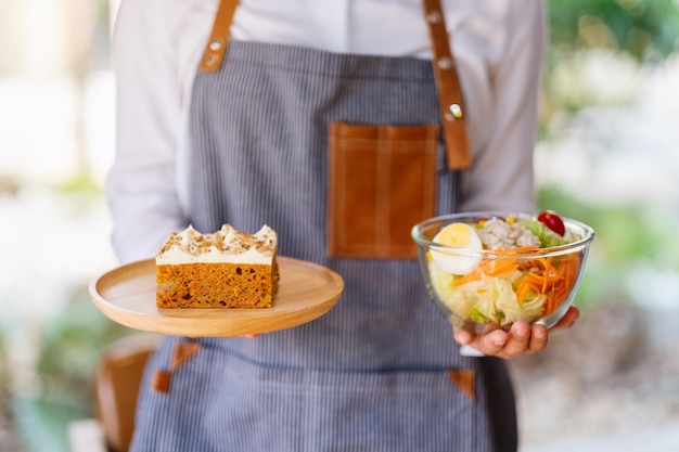 Une serveuse tenant et servant une assiette de gâteau aux carottes et un bol de salade de légumes