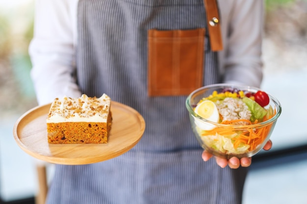 Une serveuse tenant et servant une assiette de gâteau aux carottes et un bol de salade de légumes