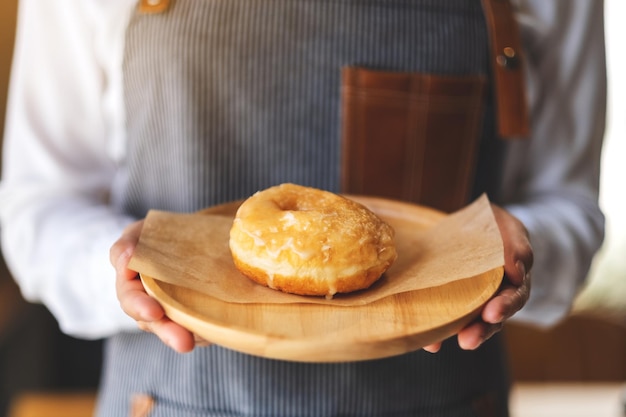 Une serveuse tenant et servant un morceau de beignet fait maison dans un plateau en bois