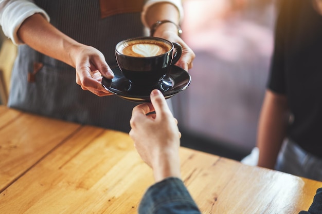 Une serveuse tenant et servant une tasse de café chaud à un client masculin au café