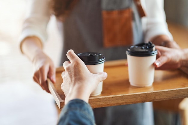 Une serveuse tenant et servant des tasses en papier de café chaud au client au café