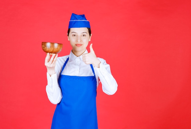 Serveuse en uniforme debout avec un bol en bois et montrant le pouce vers le haut.