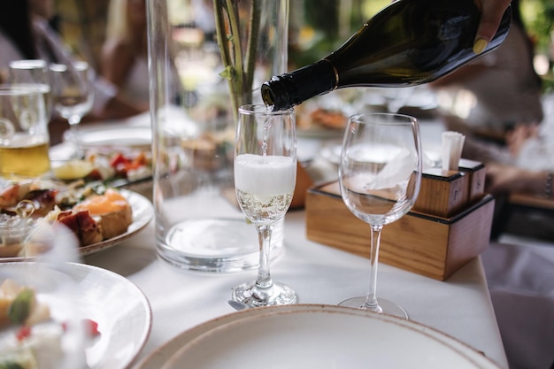 Serveuse versant du champagne sur fond de verre de personnes en train de dîner sur la terrasse d'été au café