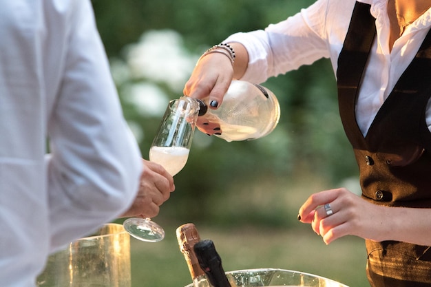Serveuse versant du vin mousseux dans un verre d'un invité lors d'une fête avant le toast