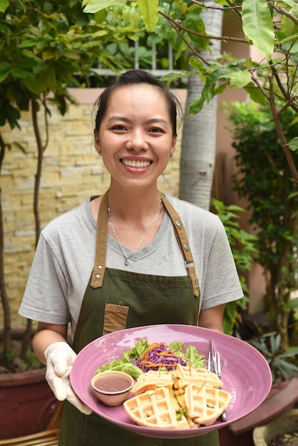 Serveuse vietnamienne servant des gaufres belges avec des légumes verts et du poulet dans un café en plein air