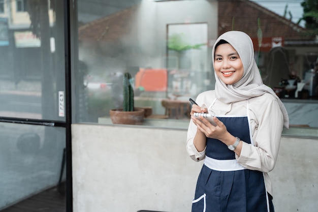 Serveuse voilée de café debout avec tenir un stylo et note