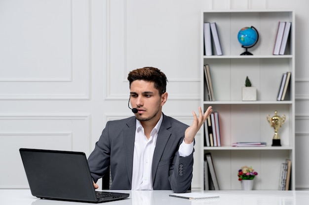 Service client mignon beau mec en costume de bureau avec ordinateur sur le casque parlant