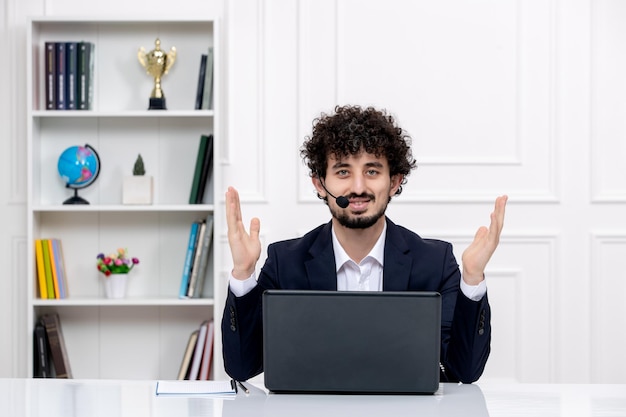 Service client mignon mec brune en costume de bureau avec ordinateur portable et casque agitant les mains