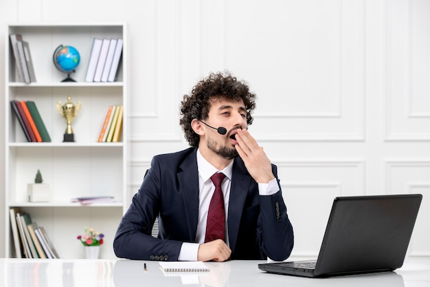 Service à la clientèle beau jeune homme en costume de bureau avec ordinateur portable et casque bâillant et fatigué