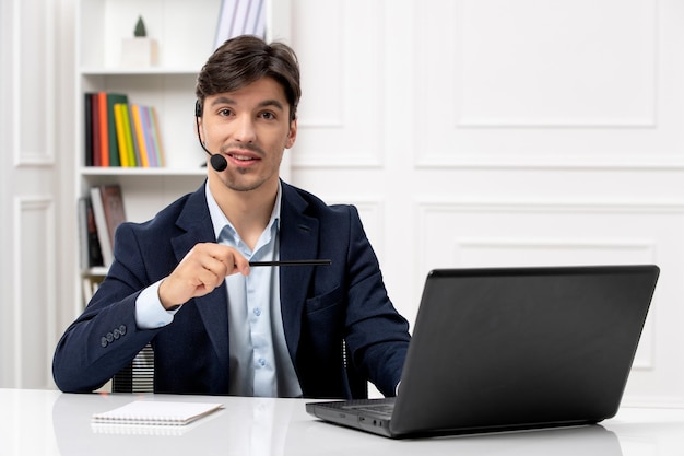 Service à la clientèle beau mec avec casque et ordinateur portable en costume pointant avec un stylo sur l'écran