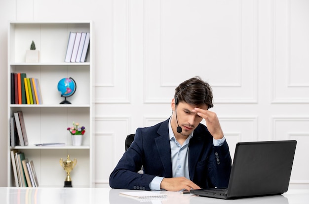 Service à la clientèle le joli mec brune en costume avec un ordinateur portable pensant et portant un casque