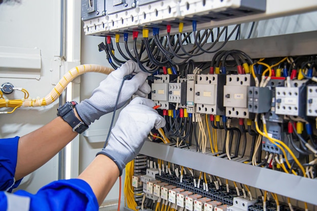 Photo service d'électricité et de maintenance électrique main d'ingénieur tenant un voltmètre ca vérifiant la tension du courant électrique à la borne du disjoncteur et au tableau de distribution d'alimentation principal du câblage du câble