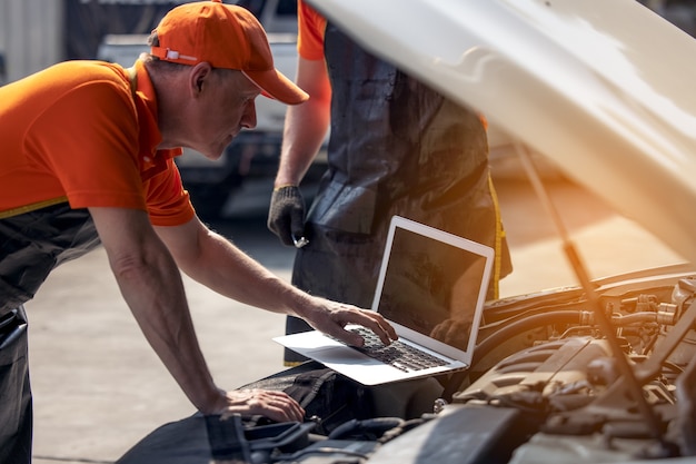 Service d'entretien de voiture, technicien diagnostique le problème de panne de moteur de voiture par ordinateur portable.