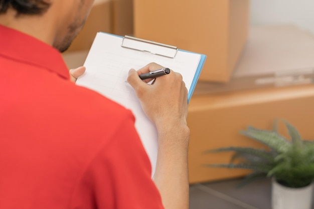 Photo service, livraison homme asiatique, liste de vérification masculine, colis ou boîte en carton, carton dans l'entrepôt avant livraison à l'adresse du client. courrier travaillant en uniforme. emménagement dans un nouveau déménagement.