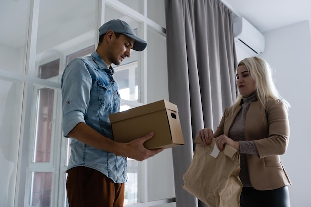 Photo service rapide et fiable. enthousiaste jeune livreur donnant une boîte en carton à une jeune femme debout à l'entrée de son appartement