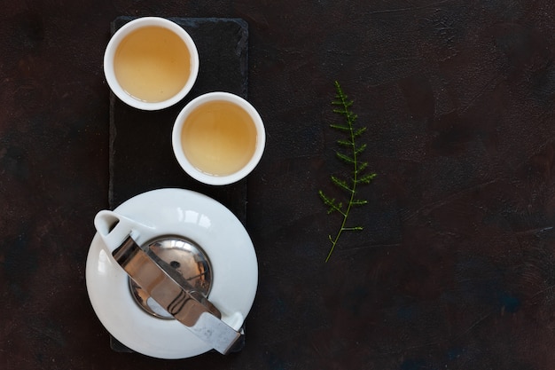 Service à thé asiatique en porcelaine blanche avec thé vert Oolong au lait sur un bureau en pierre noire