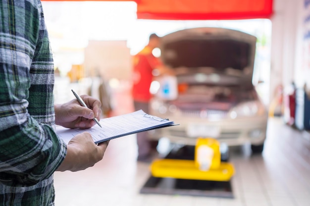 Photo services concept de machine de moteur de voiture mécanicien automobile réparateur vérifiant un moteur de voiture en inspectant l'écriture dans le presse-papiers de la liste de contrôle pour l'entretien et la maintenance de la machine de réparation