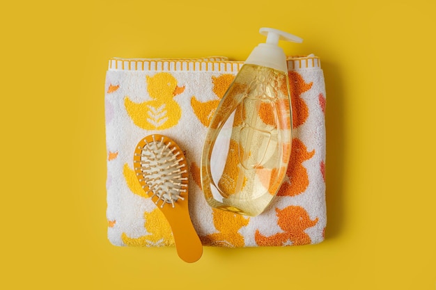 Serviette de bébé avec canards mignons et bouteille de savon ou de shampoing avec brosse à cheveux sur fond jaune. Accessoires de bain