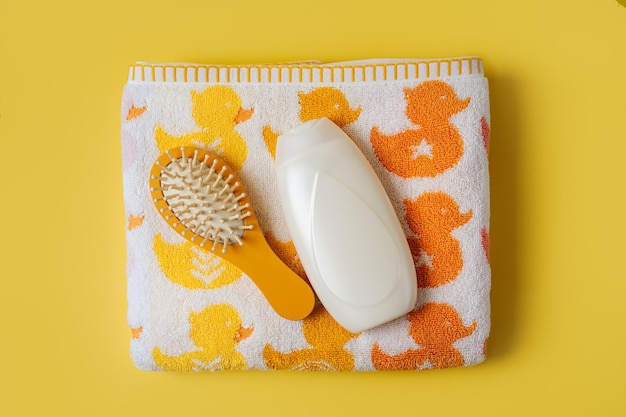 Serviette de bébé avec canards mignons et bouteille de savon ou de shampoing avec brosse à cheveux sur fond jaune. Accessoires de bain