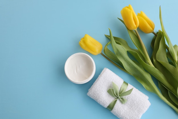 Serviette crème cosmétique et tulipe jaune sur fond bleu