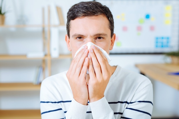 Serviette douce. Personne de sexe masculin malade portant un pull rayé et se tenant la main tout en se sentant mal