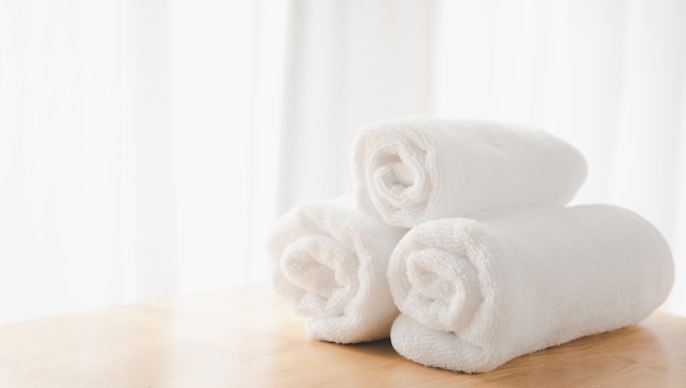 Serviettes blanches propres se plient sur une table en bois avec fond de salle de bain blanc flou